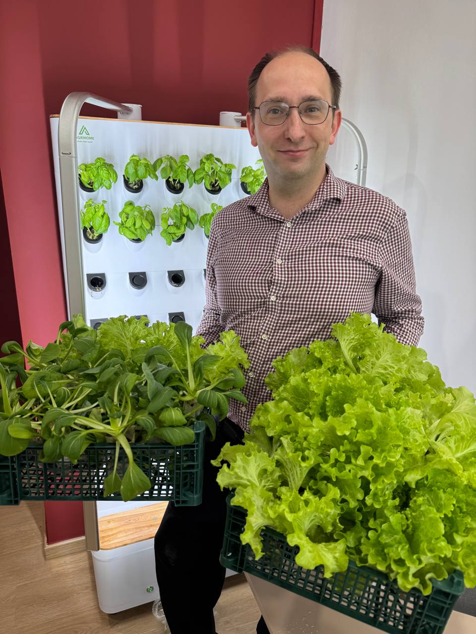 teacher holding baskets of freshly harvested green leafy vegetables with an indoor farming system from Agrihome in the background.
